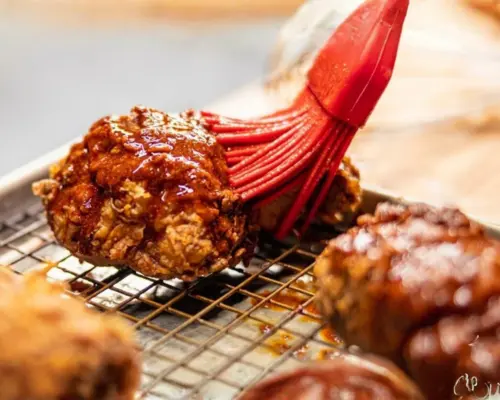 KFC Nashville Hot Tenders Combos Price & Calories 2026 12 Brushing a spicy, glistening red oil glaze over fried chicken to achieve the authentic heat of KFC Nashville Hot Tenders.