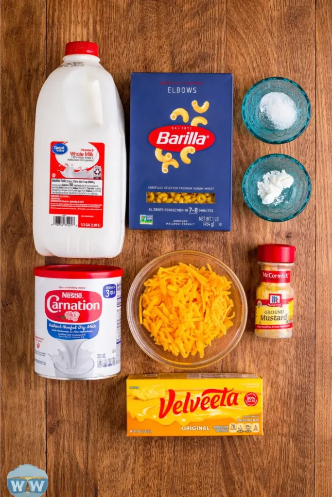 Copycat KFC Mac and Cheese Recipe, Calories & Nutrition Guide 2026 4 Ingredients for homemade KFC Mac and Cheese laid out on a wooden surface, including whole milk, dry milk, elbow macaroni, shredded cheddar, Velveeta cheese, cornstarch, and ground mustard.