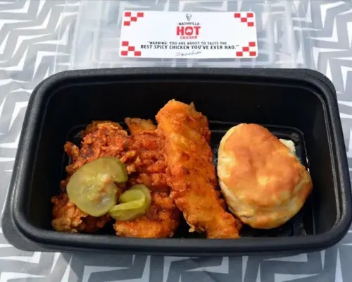 KFC Nashville Hot Chicken Combos are Back in 2026 10 A takeout container holding a complete meal of KFC Nashville Hot Tenders, a golden biscuit, and pickles on a chevron background.